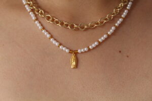 Cadena con dije de virgencita hecho en oro golfi expuesta por el cuello de una hermosa mujer