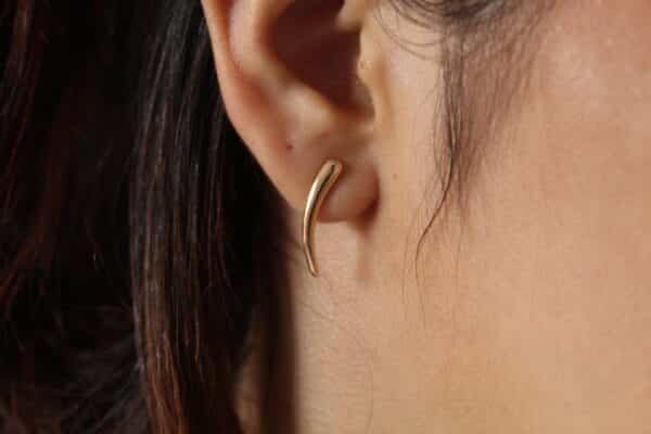 Aretes en forma de lagrima expuestos en la oreja de una hermosa mujer hechos en oro golfi