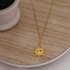 Cadena en forma de solecito expuesta en una mesa con una flor de fondo hecha en oro golfi