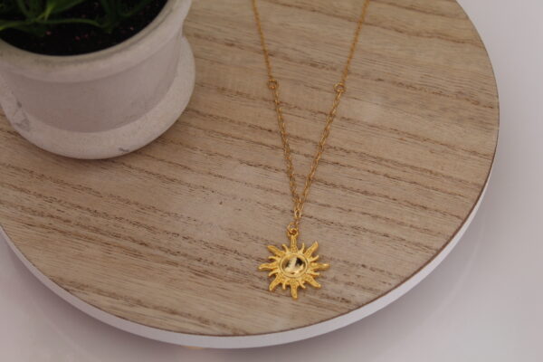 Cadena en forma de solecito expuesta en una mesa con una flor de fondo hecha en oro golfi