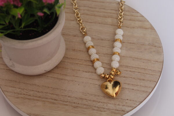 Cadena de perlas hecha con un corazon en oro golfi y expuesta en una mesa con una flor de fondo