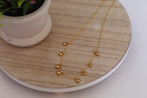 cadena_corazoncitos_mesa Cadena en forma de corazoncitos expuesta en una mesa con una flor de fondo hechas en oro golfi