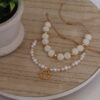 pulseras_perlas_brillantes_mesa Pulsera en forma de perlas hecha con oro golfi expuesta en una mesa con una flor de fondo