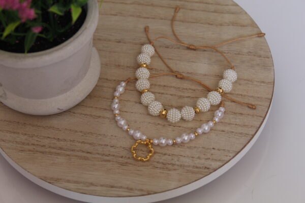 pulseras_perlas_brillantes_mesa Pulsera en forma de perlas hecha con oro golfi expuesta en una mesa con una flor de fondo