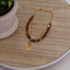 pulsera_ancla Pulsera en forma de ancla hecha en oro golfi expuesta en una mesa con una flor de fondo