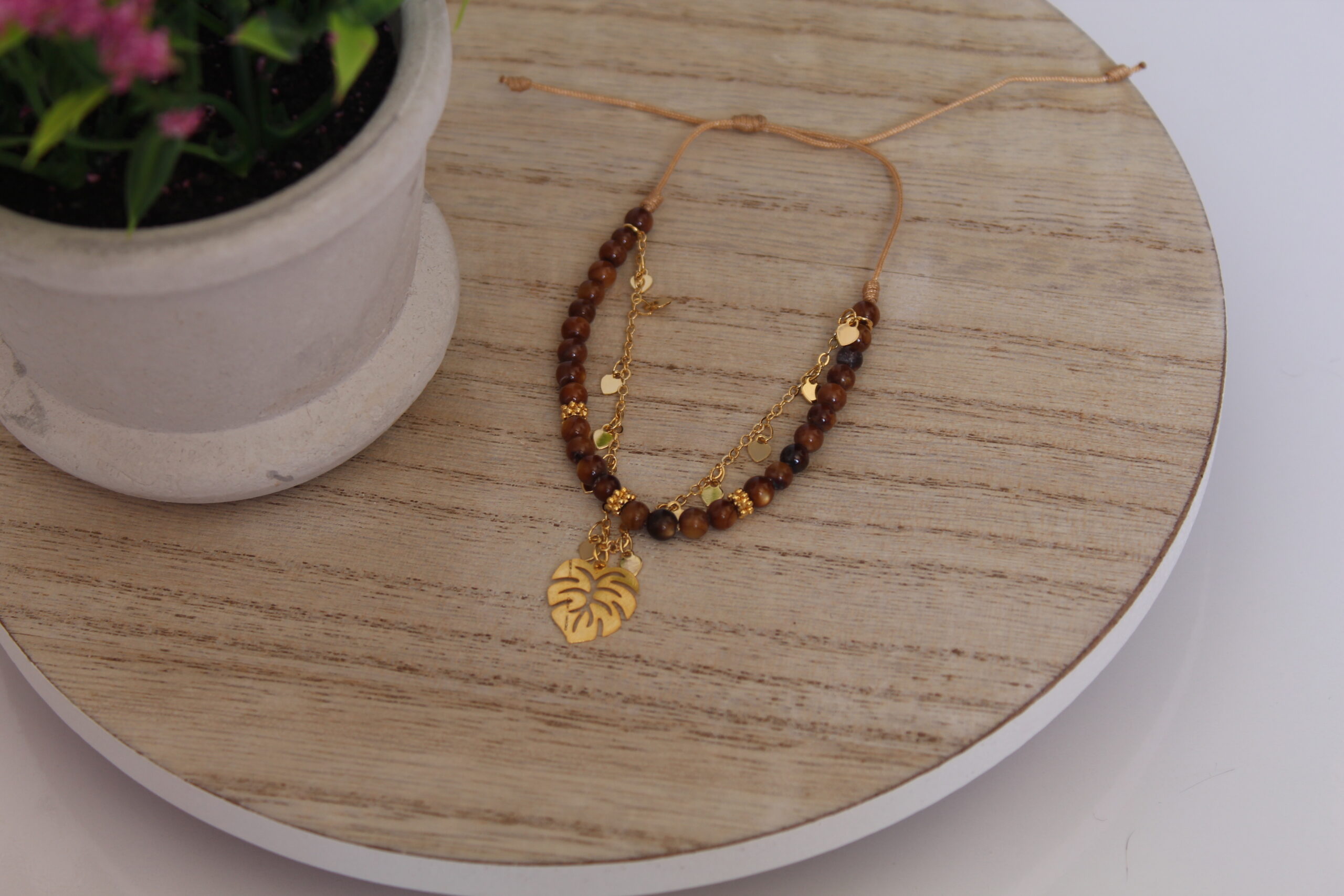 pulsera_ancla Pulsera en forma de ancla hecha en oro golfi expuesta en una mesa con una flor de fondo