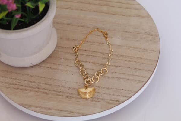 pulsera_conchita_de_mar Pulsera en forma de conchita hecha en oro golfi expuesta en una mesa con una flor de fondo