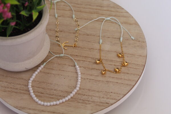 Son 3 pulseras expuestas en una mesa con una flor las cuales son echas en oro golfi muy delicadas