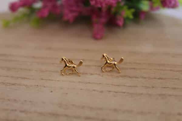 Aretes en forma de caballo hechos en oro golfi expuestos en una mesa con una flor de fondo