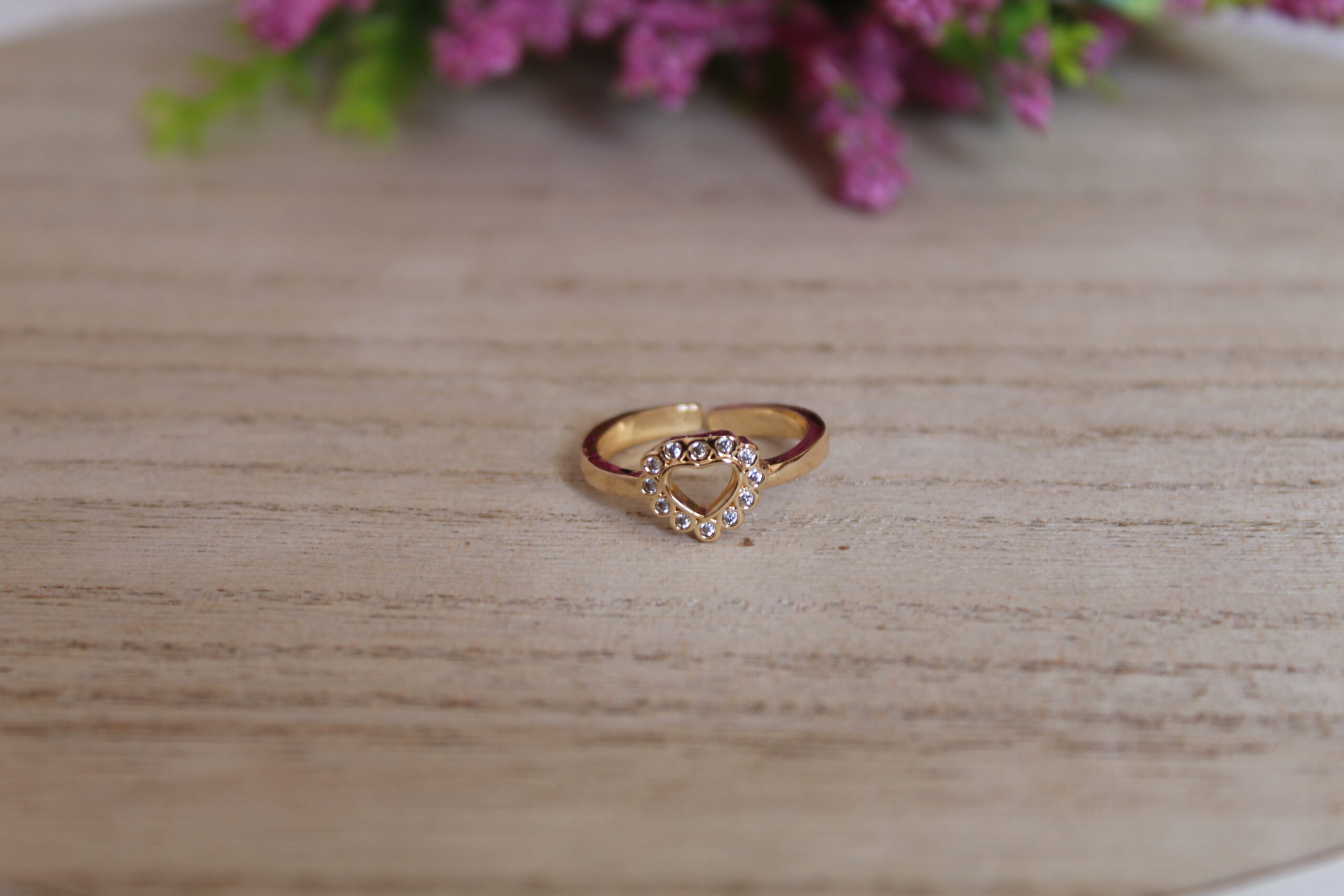 anillo_de_corazon Anillo con forma de corazon echo en oro golfi y con perlas brillantes el cual esta puesto en una mesa con una flor de fondo