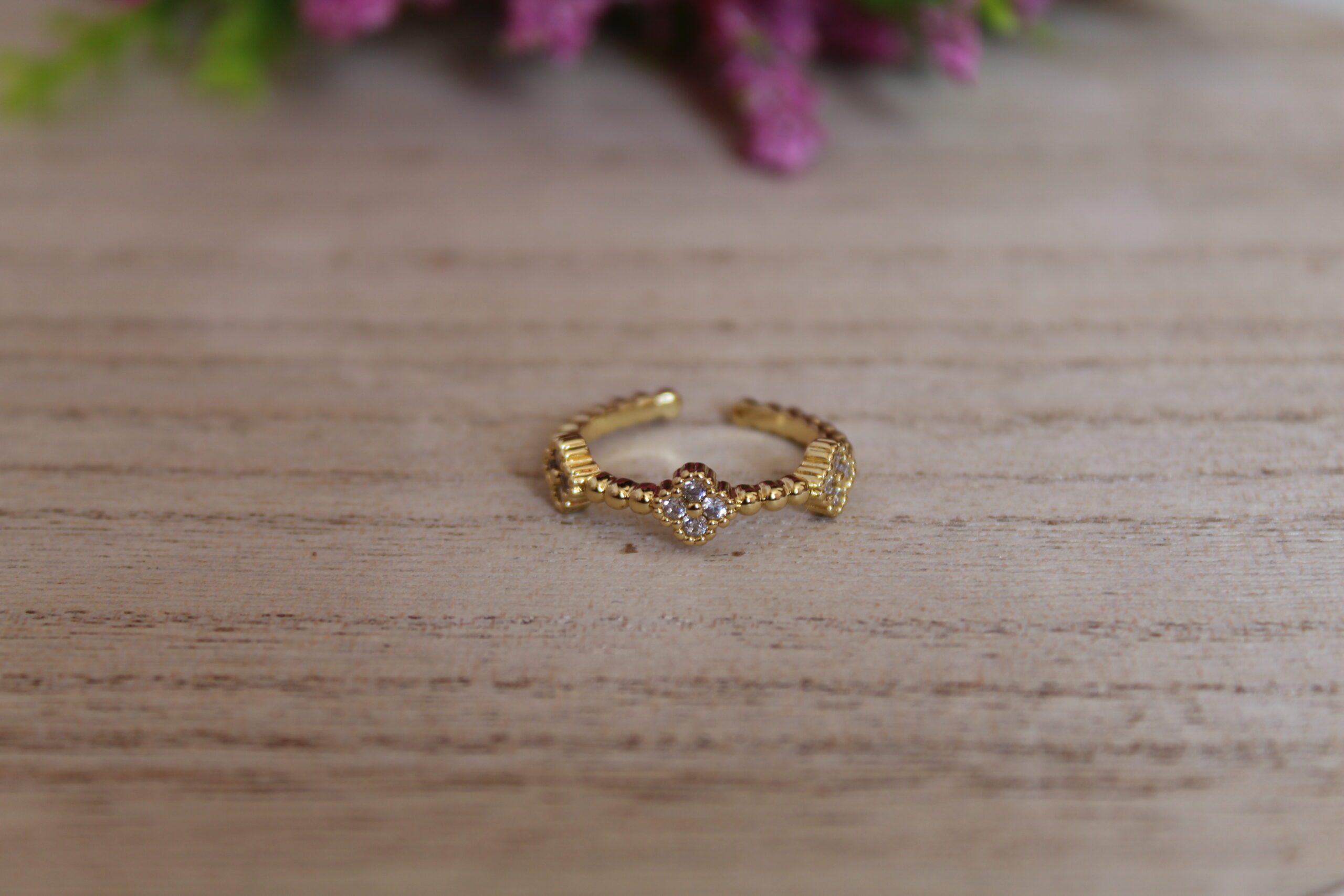 anillo_trebol Anillo en forma de trébol echo en oro golfi y perlas brillantes el cual esta puesto encima de una mesa con una flor de fondo