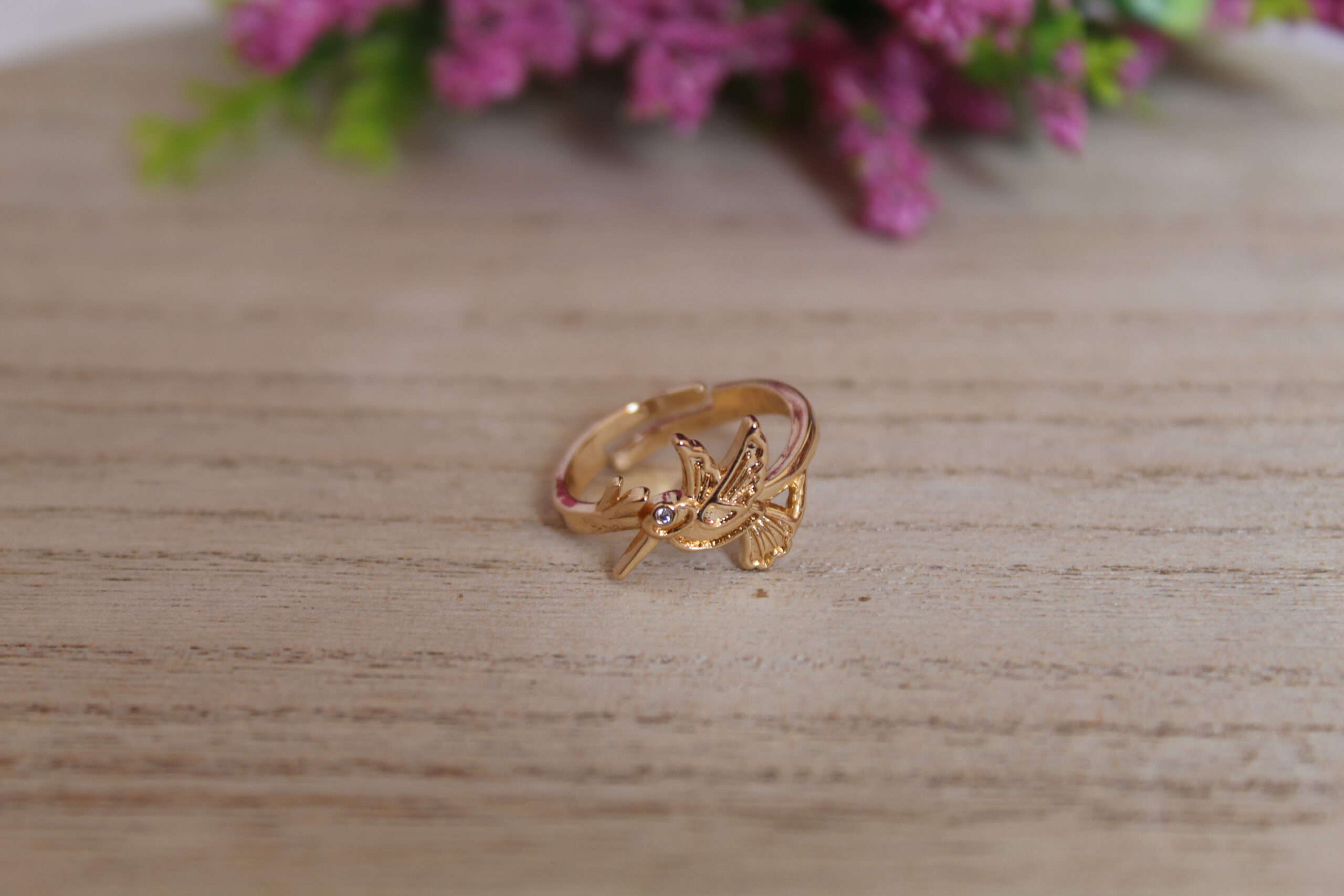 anillo_colibri Anillo echo en oro golfi con forma de colibri puesto en una mesa con una flor de fondo